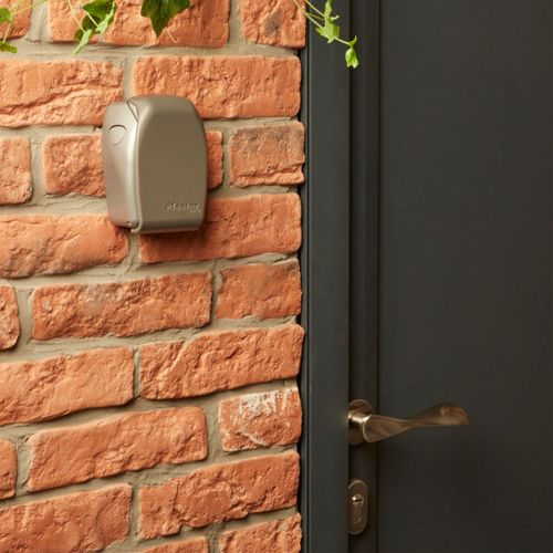 Un alloggiamento grigio su un muro di mattoni accanto a una porta scura con maniglia in ottone.