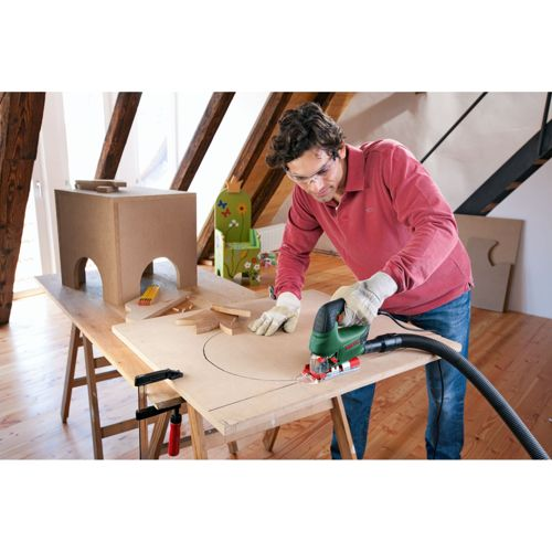 Hombre cortando tablero de madera con sierra de calar en mesa de madera.