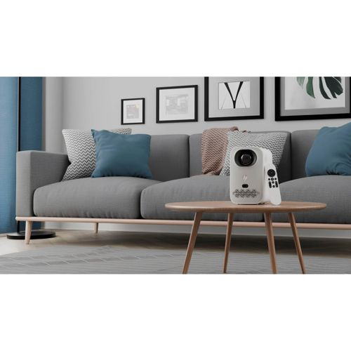Ein weißer Projektor mit Fernbedienung steht auf einem Holztisch vor einem grauen Sofa mit Kissen.