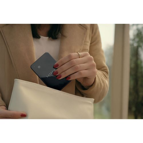 Eine Frau mit roten Nägeln legt ein schwarzes Gerät in eine cremefarbene Tasche.