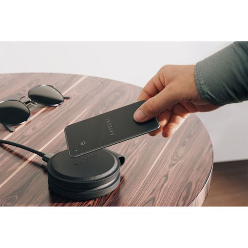 Hand legt schwarzes Satechi-Telefon auf schwarzen kabellosen Lader auf Holztisch.
