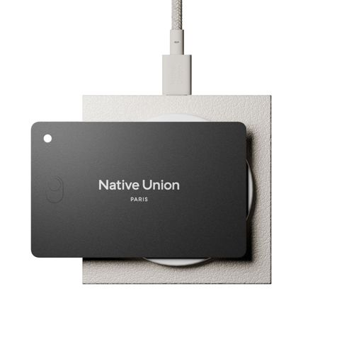 Ein schwarzes Native Union Ladeetui liegt auf einer weißen Ladeplatte. Ein Kabel ist angeschlossen.