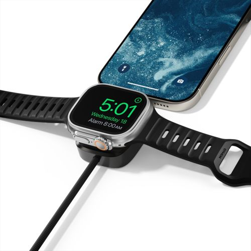 Uno smartwatch argentato con cinturino nero si carica su un supporto nero accanto a uno smartphone.