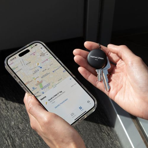 Hände halten ein Handy mit Karten-App und Schlüssel mit rundem Tracker.