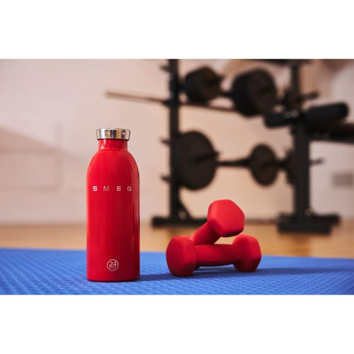 Kırmızı SMEG şişesi ve dambıllar spor salonunda mavi mat üzerinde.