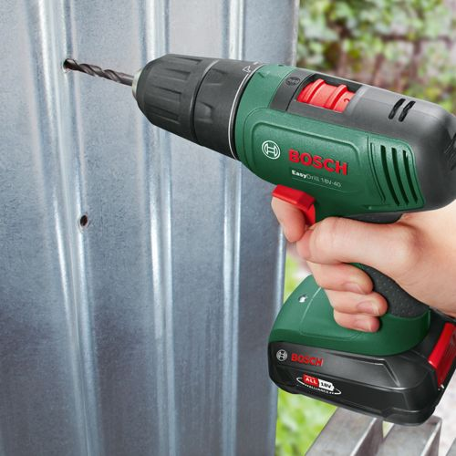 Una mano tiene un trapano Bosch verde che fa un foro nel metallo.