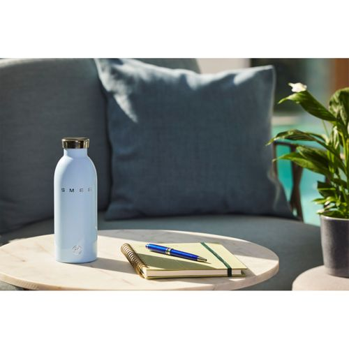 Hellblaue Smeg-Flasche auf einem Marmortisch mit Notizbuch und Stift.