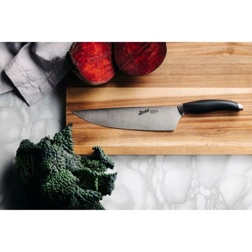 Un coltello da chef poggia su un tagliere di legno accanto a barbabietole e cavolo nero.