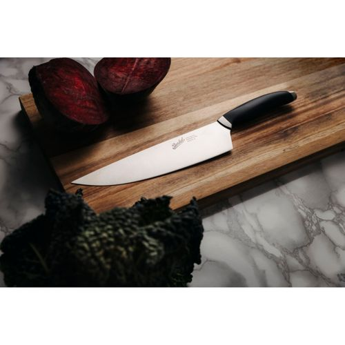 Un coltello da chef poggia su un tagliere di legno accanto a due barbabietole tagliate e cavolo nero scuro.