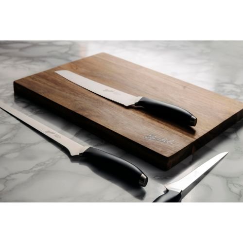 Tre coltelli con manici neri su tagliere in legno, su superficie in marmo.
