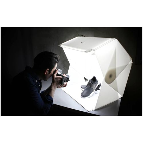 Mann fotografiert schwarze Schuhe in einem aufklappbaren Fotostudio mit Lichtern.