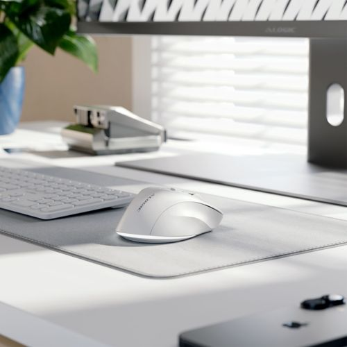 Un mouse bianco su un tappetino grigio accanto a una tastiera e una spillatrice.