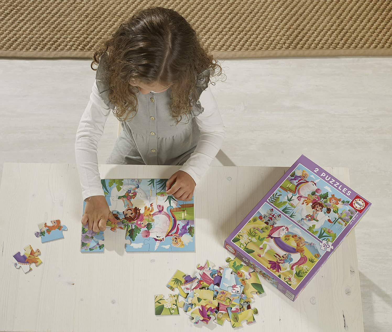 Una niña arma un rompecabezas de unicornio en una mesa de madera. Una caja de rompecabezas está cerca.