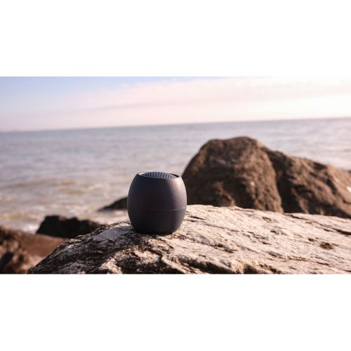 Une enceinte ovale foncée est posée sur des rochers au bord de la mer.