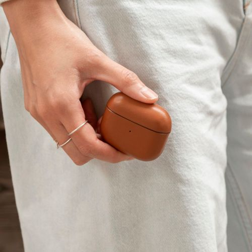 Eine Hand hält ein braunes Ladecase für Kopfhörer vor einer Jeans.