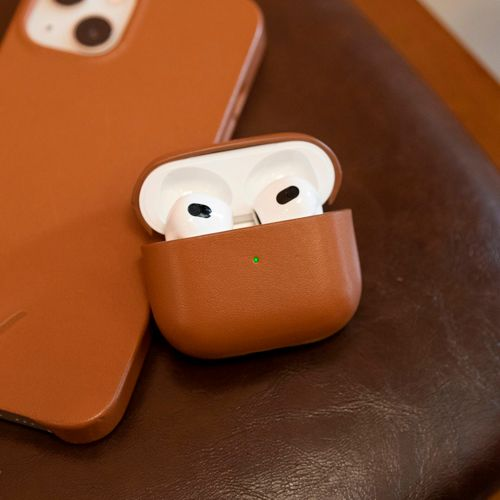Braune Lederhülle mit weißen Kopfhörern und einem darunter liegenden Handy.