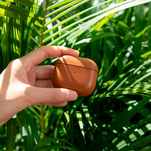 Eine Hand hält eine braune Leder-Ohrhörerhülle mit grünen Blättern im Hintergrund.