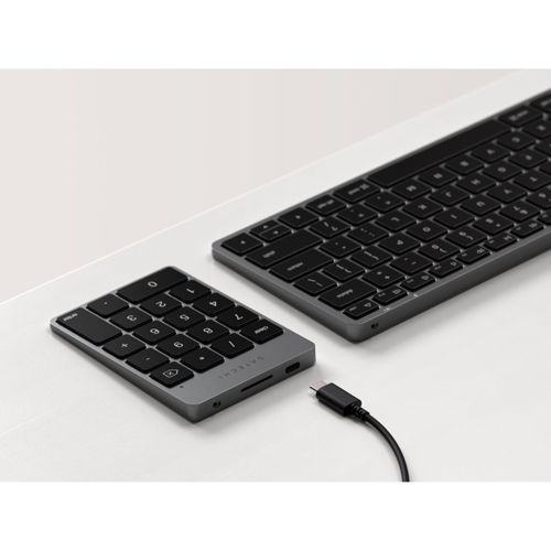 Un teclado numérico gris y un teclado están uno al lado del otro en un escritorio blanco.
