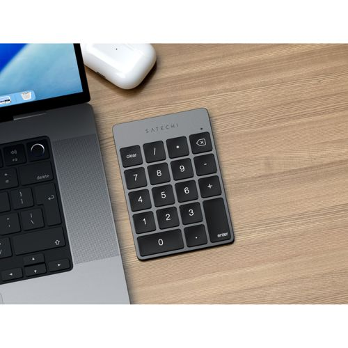 Un teclado Satechi y un portátil están sobre un escritorio de madera junto a un ratón inalámbrico blanco.
