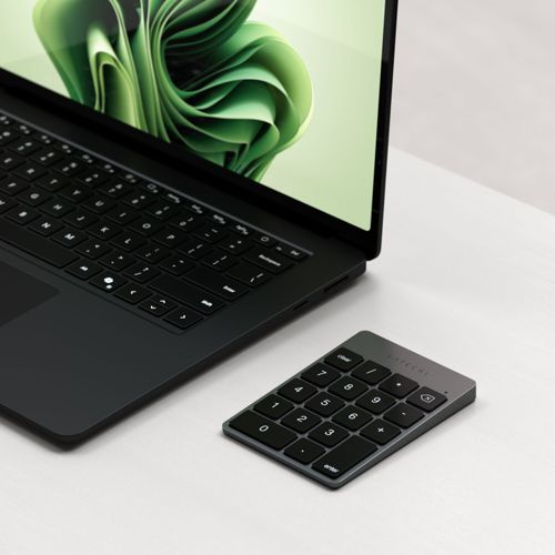 Un portátil negro con fondo de escritorio verde y un teclado numérico separado.