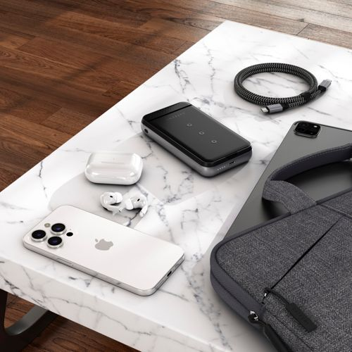 Un iPhone blanco, auriculares blancos, estuche de carga, batería externa y cable en mesa mármol.