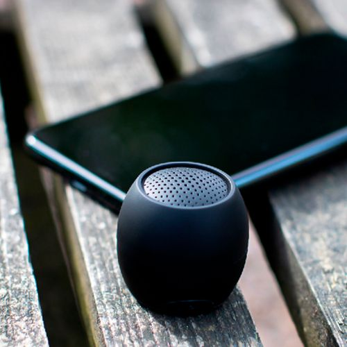 Kleine zwarte luidspreker en een smartphone op een houten bankje.