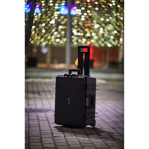 Ein schwarzer Rollkoffer steht auf gepflastertem Untergrund, im Hintergrund Bokeh-Lichter.