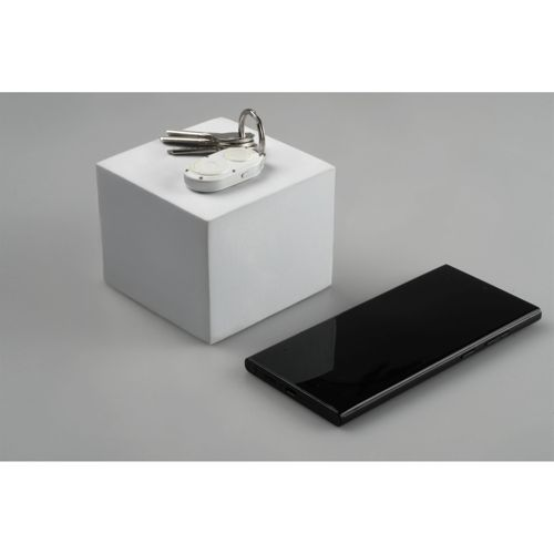 Black smartphone lies next to a white cube with keys and a white keychain.