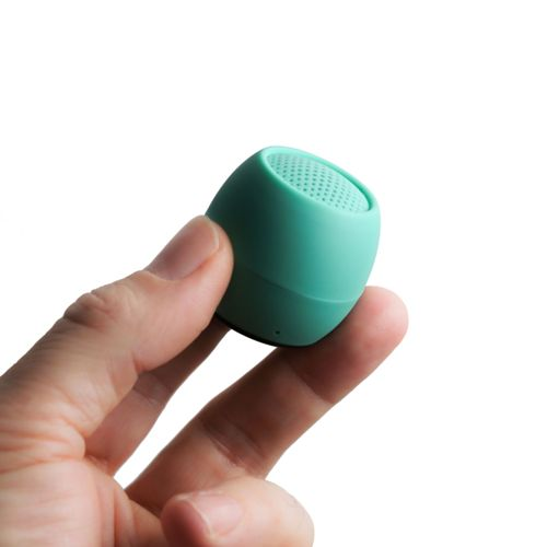 Una mano tiene un piccolo altoparlante Bluetooth verde acqua con una griglia perforata in alto.