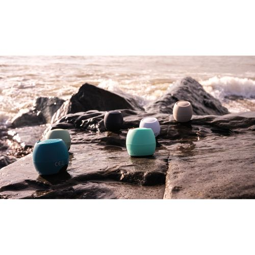 Diversi altoparlanti colorati riposano su rocce bagnate vicino al mare.