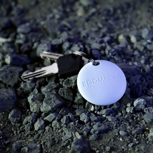 Un portachiavi rotondo bianco con logo BOOMPODS giace sulle pietre.