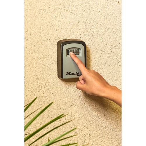 Una mano presiona un número en una caja fuerte de llaves Master Lock en una pared.