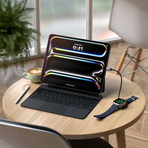 Un tablet con tastiera, stilo, caffè e un orologio in carica su un tavolo di legno.