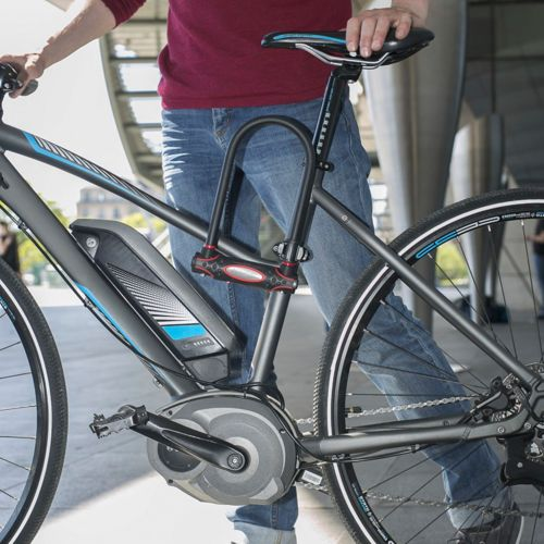 Ein Mann in Jeans und rotem Hemd schließt ein E-Bike mit einem Bügelschloss ab.