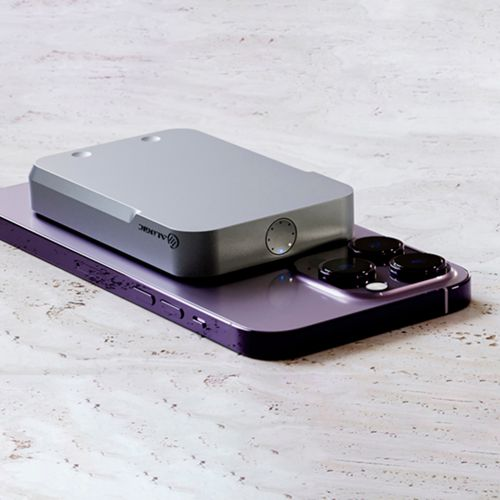 Ein silbernes Gerät liegt auf einem violetten Smartphone. Nahaufnahme.