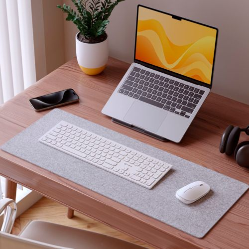 Una scrivania in legno con laptop, tastiera, mouse, cuffie, telefono e pianta.