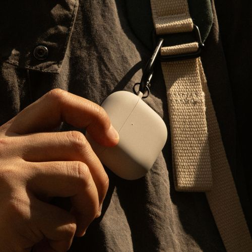 Una mano tiene una custodia grigio chiaro per auricolari wireless attaccata a una cinghia.