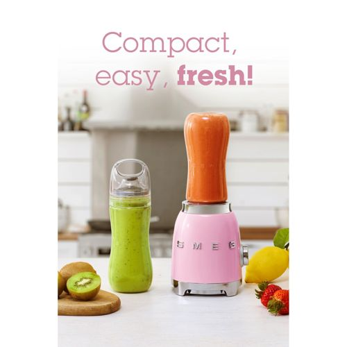 Un frullatore rosa con succo d'arancia e bottiglia di smoothie verde. Kiwi e fragole vicini.