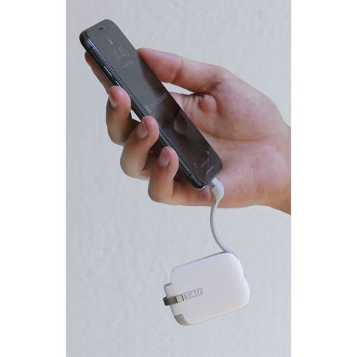 Una mano tiene uno smartphone collegato a un cavo di ricarica bianco.