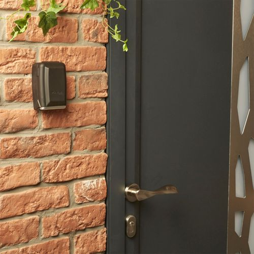 Una caja oscura en una pared de ladrillos junto a una puerta gris con un tirador plateado.