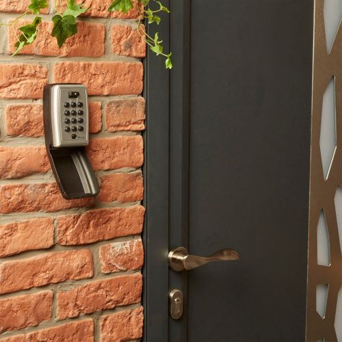 Un teclado de acceso en una pared de ladrillos junto a una puerta oscura con pomo de latón.