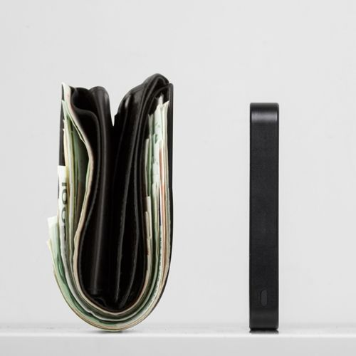 Un portefeuille noir rempli de billets se trouve à côté d'un objet noir fin.