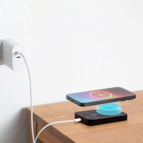 Un smartphone se charge sans fil sur une station de charge noire.