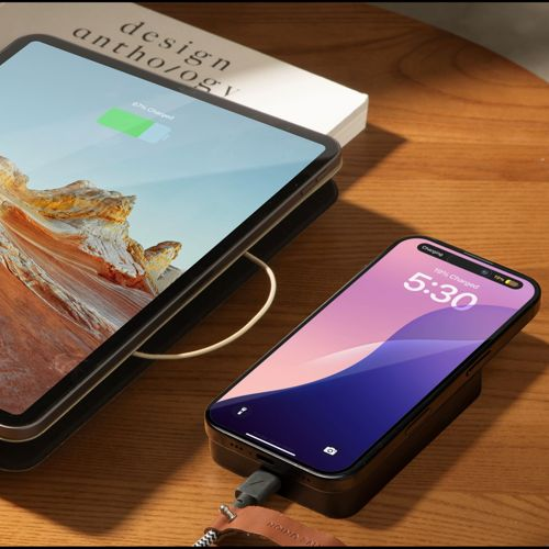 Une tablette et un smartphone chargent sur une table en bois à côté d'un livre.