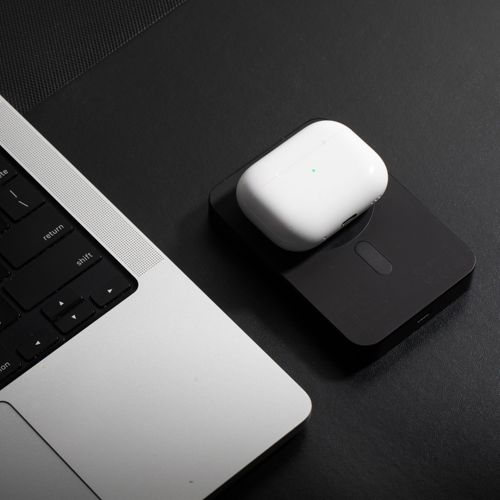 Un étui blanc pour écouteurs sans fil repose sur un chargeur noir à côté d'un ordinateur portable.