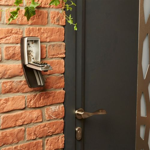Una caja de llaves con combinación cuelga de una pared de ladrillos junto a una puerta oscura.
