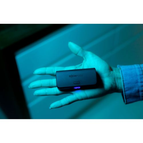 Eine Hand hält ein kleines schwarzes BOOMPODS-Gerät mit blauer Anzeige.