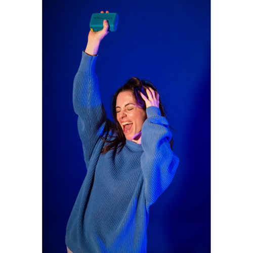 Une femme en pull bleu tient un objet bleu au-dessus de sa tête, sur fond bleu.