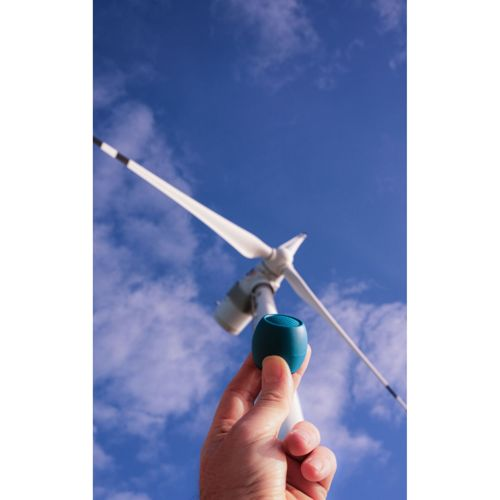 Main tenant un petit objet bleu devant une éolienne et un ciel bleu avec nuages.
