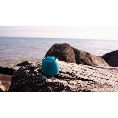 Une enceinte turquoise repose sur un rocher au bord de la mer.